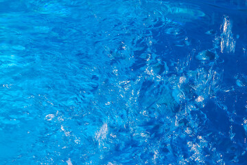superficie del agua turquesa de una piscina con los reflejos del sol sobre el agua azul