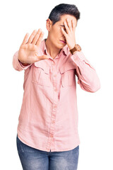 Young woman with short hair wearing casual clothes covering eyes with hands and doing stop gesture with sad and fear expression. embarrassed and negative concept.