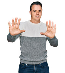 Handsome young man wearing casual winter sweater afraid and terrified with fear expression stop gesture with hands, shouting in shock. panic concept.