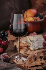 Glass of red wine served with blue cheese on dark wooden background. Autumn picnic with wine and cheese platter, fruits and dry leaves in rustic style