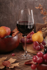 Glass of rich red wine served with fruits on dark wooden background. Autumn still life with wine, grapes and dry leaves in rustic style. Sweater weather concept