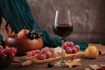 Glass of red wine served with blue cheese on dark wooden background. Autumn picnic with wine and cheese platter, fruits and dry leaves in rustic style