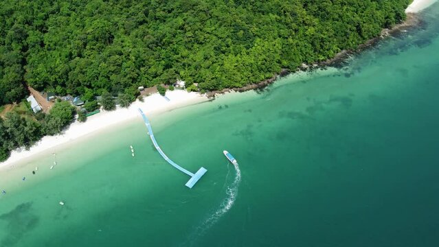 Aerial bird view of small boat arriving at tropical island showing the beautiful shallow blue green ocean water and the white beach and palm trees amazing paradise vacation location 4k quality