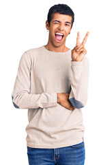 Young african amercian man wearing casual clothes smiling with happy face winking at the camera doing victory sign. number two.