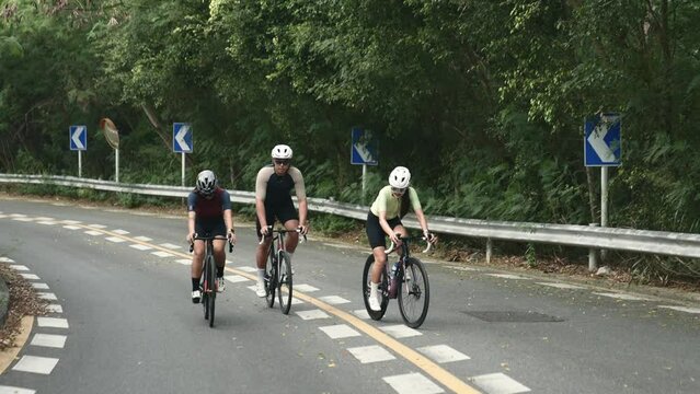 three young asian cyclists riding bicycle on a uphill country road