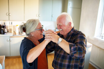 Happy elderly couple dancing and holding hands at home kitchen