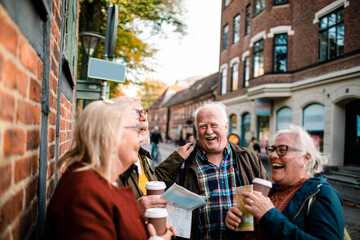 Group of senior friends with map and coffee laughing together on city street