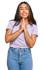 Fototapeta premium Young latin woman wearing casual clothes praying with hands together asking for forgiveness smiling confident.