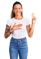 Obraz premium Young hispanic woman with tattoo wearing casual white tshirt smiling swearing with hand on chest and fingers up, making a loyalty promise oath