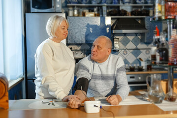 An elderly woman measures her husband's blood pressure and pulse.