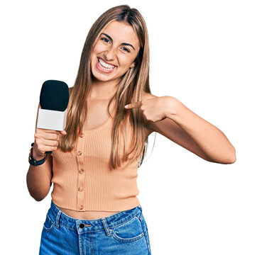 Hispanic young woman holding reporter microphone pointing finger to one self smiling happy and proud