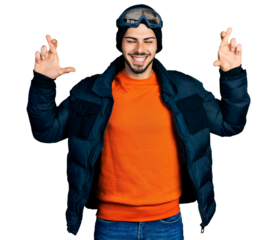 Young hispanic man with beard wearing snow wear and sky glasses gesturing finger crossed smiling with hope and eyes closed. luck and superstitious concept.