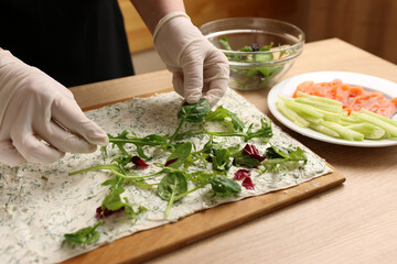 Greens are added to pita bread with cheese. Preparation of a roll with cheese, fish and vegetables