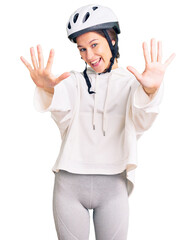 Beautiful brunette young woman wearing bike helmet and sporty clothes showing and pointing up with fingers number ten while smiling confident and happy.