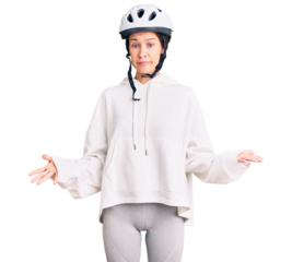 Beautiful brunette young woman wearing bike helmet and sporty clothes clueless and confused expression with arms and hands raised. doubt concept.