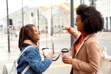 Two african woman friends drinking coffee outdoor, smiling and talking.