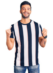 Young handsome hispanic man wearing striped tshirt celebrating surprised and amazed for success...