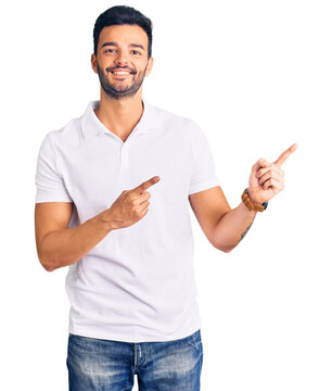 Young handsome hispanic man wearing casual clothes smiling and looking at the camera pointing with two hands and fingers to the side.