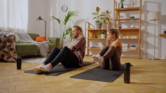 Sportive couple sitting on yoga mats and doing abs exercise
