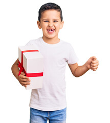 Little cute boy kid holding gift screaming proud, celebrating victory and success very excited with...