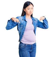 Young beautiful chinese woman pregnant expecting baby pointing down looking sad and upset,...