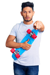 Handsome latin american young man holding skate pointing with finger to the camera and to you,...