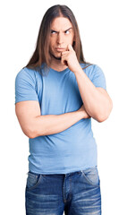 Young adult man with long hair wearing casual clothes serious face thinking about question with hand on chin, thoughtful about confusing idea