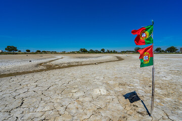 dry and cracked floor of dry river with portuguese national flag