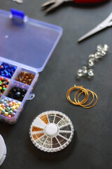 Box with colorful beads, string, wire, chain, scissors, pliers and hammer on dark background. Various jewelry making supplies. Selective focus.