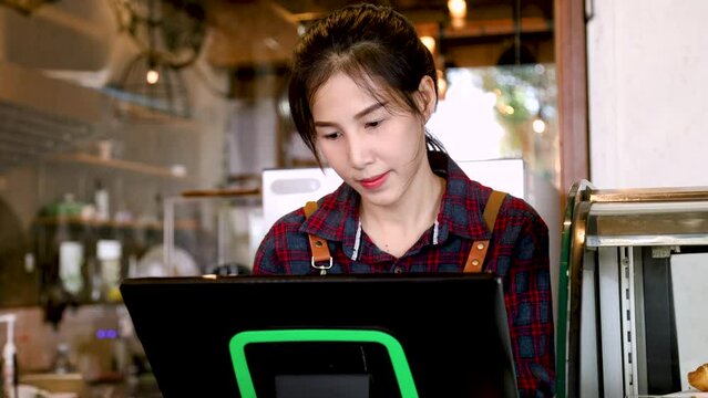 Asian retail small business owner female taking customer order using modern POS purchasing order system machine making selling transaction standing in counter, barista waitress worker happy smiling