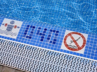 A close-up view of a pool border indicating the pool's depth and signs regulating behavior in the pool. Spain.