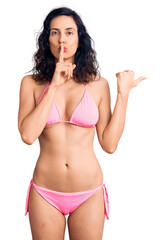 Young beautiful hispanic woman wearing bikini asking to be quiet with finger on lips pointing with hand to the side. silence and secret concept.