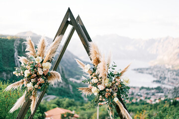 Triangular wedding tipi arch decorated with flowers stands on a mountain above the Kotor Bay....