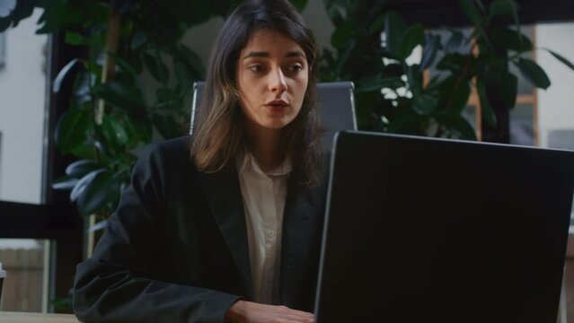 Businesswoman uses laptop to connect with clients discussing project updates at online meeting. Concentrated woman uses device to conduct virtual meeting discussing project requirements