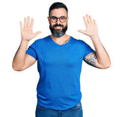 Hispanic man with beard wearing casual t shirt and glasses showing and pointing up with fingers number ten while smiling confident and happy.