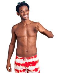 Fototapeta premium African handsome man wearing swimsuit and sunglasses doing happy thumbs up gesture with hand. approving expression looking at the camera showing success.