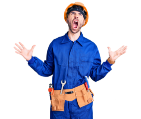Young hispanic man wearing worker uniform crazy and mad shouting and yelling with aggressive expression and arms raised. frustration concept.