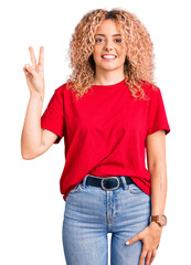 Young blonde woman with curly hair wearing casual red tshirt showing and pointing up with fingers number two while smiling confident and happy.