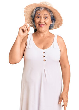 Senior woman with gray hair wearing summer hat and summer clothes pointing finger up with successful idea. exited and happy. number one.