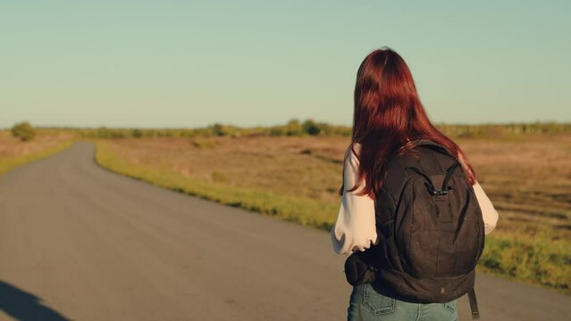 girl traveling with backpack sunset, family sun, hiking girl asphalt road, back view woman traveling on an autumn road with backpack, raises her hands up, walking above sunlight, attractive happy