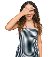 Obraz na płótnie Canvas Teenager hispanic girl wearing casual clothes peeking in shock covering face and eyes with hand, looking through fingers with embarrassed expression.