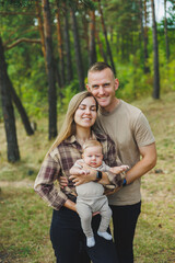 Happy young mother and father with a child on a walk in the park. The concept of a happy married couple with a child. Happy family couple with little newborn son in nature.