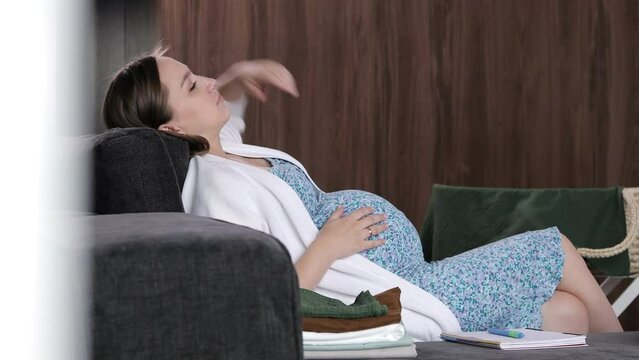 Pregnant woman strokes her stomach, after which she wants to get up from the sofa