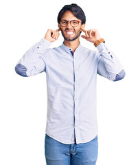 Handsome hispanic man wearing business shirt and glasses covering ears with fingers with annoyed expression for the noise of loud music. deaf concept.