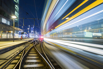 Fototapeta na wymiar Lichtspuren der Mobilität: Ein langzeitbelichteter Blick auf einen Bahnhof, mit faszinierenden Lichtstreifen von vorbeifahrenden Zügen, eine dynamische Nachtansicht der modernen urbanen Mobilität