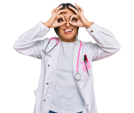 Beautiful hispanic woman wearing doctor uniform and stethoscope doing ok gesture like binoculars sticking tongue out, eyes looking through fingers. crazy expression.