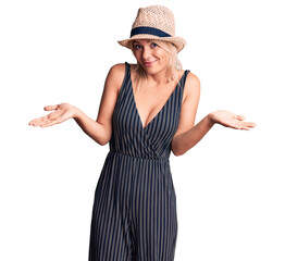 Young beautiful blonde woman wearing summer hat and dress clueless and confused expression with...