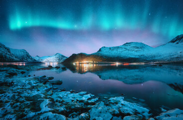 Aurora borealis over the snowy mountains, frozen sea, reflection in water at winter night in...