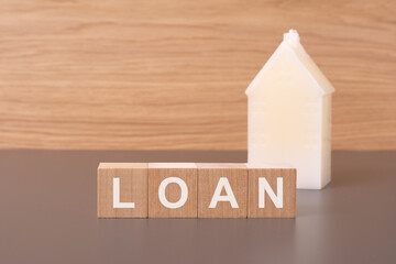 close-up of LOAN wooden cubes on brown background with toy white house