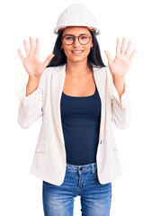 Fototapeta na wymiar Young beautiful latin girl wearing architect hardhat and glasses showing and pointing up with fingers number ten while smiling confident and happy.